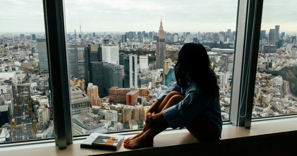 働く世代の葛藤をイメージした、オフィスの窓際で外を見つめる女性の画像