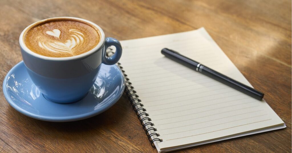 主人公が詩を書き留める「秘密のノート」をイメージした、カフェテーブルにコーヒー、ノート、ペンが置かれている画像